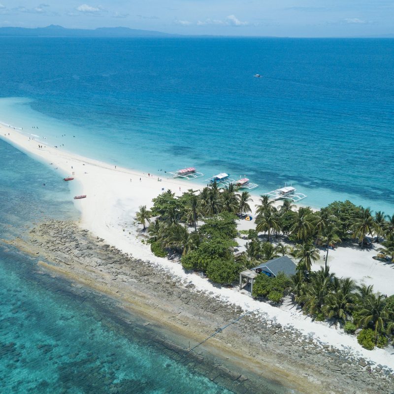 An aerial view of Kalanggaman Island, a narrow palm-covered island with white sandbars running out into clear water.